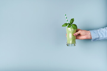 Spinach green smoothie. Vegan smoothie from spinach green, basil, chia seeds and mint in glass in hands of female on blue background. Clean eating, alkaline diet, weight loss food concept. Mock up.