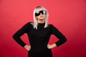 Portrait of woman standing and posing with a black glasses on a red background