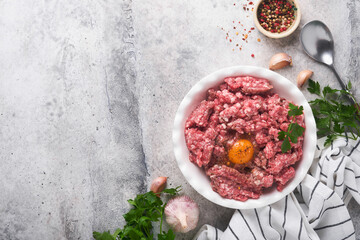 Raw minced meat. Ground meat beef, pork or lamb spices, herbs and eggs on white plate on light grey...