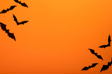 Orange Halloween background. Flock of black bats for Halloween. Black paper bat silhouettes on orange background. Halloween concept, Copy space, top view, overhead.