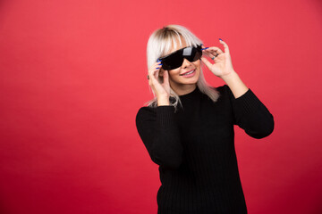 Portrait of woman putting on a black glasses on a red background