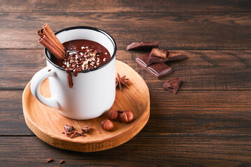 Hot chocolate. Homemade spicy hot chocolate with cinnamon, crushed hazelnut in enamel mug on old wooden background. Cozy seasonal holidays.
