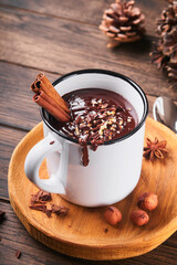 Hot chocolate. Homemade spicy hot chocolate with cinnamon, crushed hazelnut in enamel mug on old wooden background. Cozy seasonal holidays.