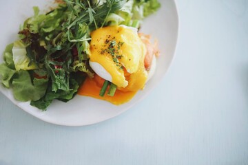 Eggs Benedict on english muffin with smoked salmon and fresh salad on table in restaurant.