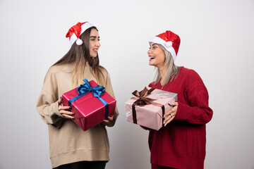 Two smiling girls in Santa hat holding festive Christmas presents