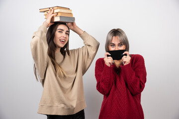 Girl in beige sweater holding books and another girl holding a smartphone