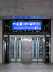 Elevator front view with glass in modern train station in Switzerland in the night. Above are the indications on a blue sign.