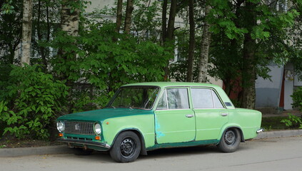 Old green Soviet car in the courtyard of a residential building, Dybenko Street, St. Petersburg, Russia, July 2022