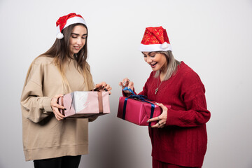 Two smiling girls in Santa hat wrapping festive Christmas presents