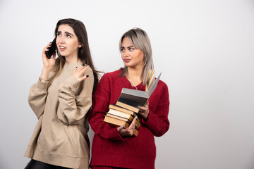 Girl in red sweater reading a book while another girl speaking on phone
