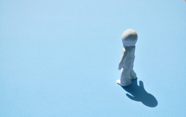 white clay man standing on sunlight with shadow on blue background