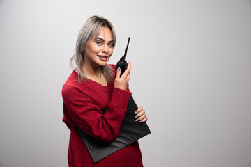 Businesswoman with clipboard and radio transceiver standing on gray background