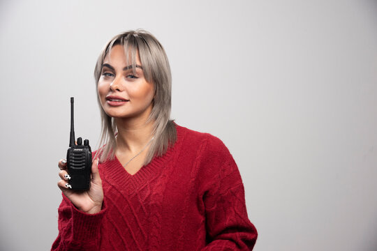 Businesswoman with radio transceiver standing on gray background