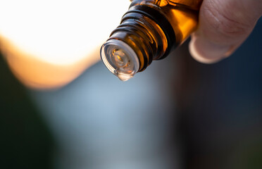 Close-up of a hand with a small, brown glass bottle dripping a liquid substance. Essential oil, medicine, homeopathy concept.