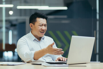 Frustrated and angry asian businessman talking on video call, man arguing and looking at laptop...