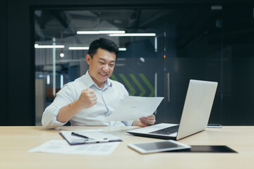 Fototapeta na wymiar Asian businessman happy with paper work, reading successful financial report, happy and celebrating victory, man in office working with documents.