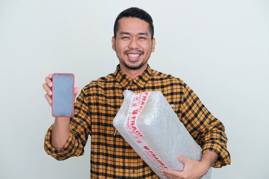 Adult Asian Man Smiling While Showing Blank Mobile Phone Screen And Holding Wrapped Package