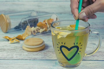 Transparent heart tea cup and female hand stirring with spoon, on a wooden table