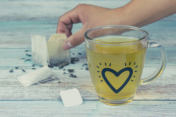 Transparent tea cup with heart and female hand, on a wooden table