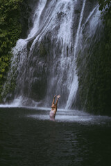 Fototapeta na wymiar A young woman swims in a mountain waterfall in Bali. Travel to Bali.