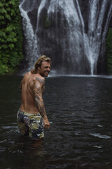 Fototapeta na wymiar Young athletic man swims in a mountain waterfall, Bali landscape, Indonesia. Tourism in Bali.