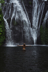 Young athletic man swims in a mountain waterfall, Bali landscape, Indonesia. Tourism in Bali.