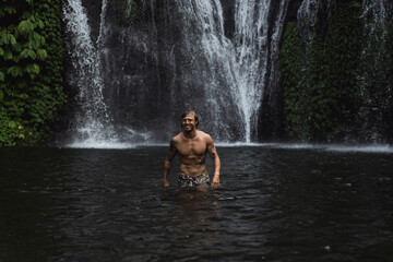 Fototapeta premium Young athletic man swims in a mountain waterfall, Bali landscape, Indonesia. Tourism in Bali.