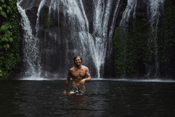 Young athletic man swims in a mountain waterfall, Bali landscape, Indonesia. Tourism in Bali.