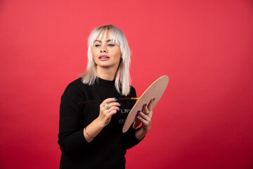 Young artist woman holding art supplies on a red background