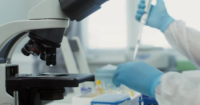 A scientist in sterile clothing looks through a microscope