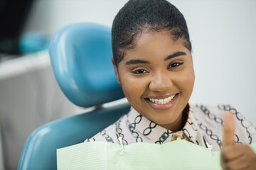 happy young woman with hand gesture in dentist chair	

