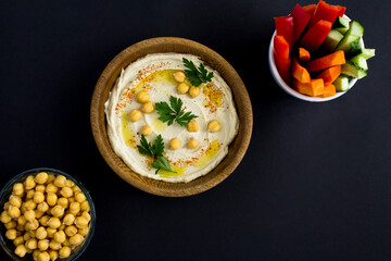 Top view of hummus in the bowl and vegetable on the black background. Closeup. Copy space.