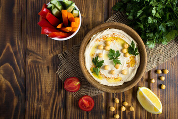 Top view of hummus in the bowl and vegetable on the rustic wooden background. Closeup. Copy space.