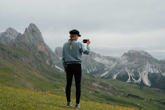 Woman overlooking Seceda in Dolomite mountains taking photos