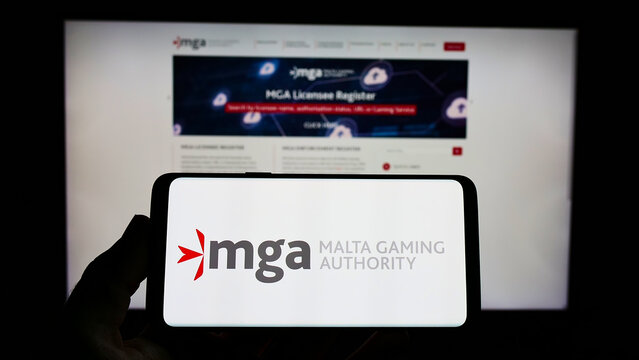 Stuttgart, Germany - 01-22-2022: Person holding smartphone with logo of Maltese institution Malta Gaming Authority (MGA) on screen in front of website. Focus on phone display.