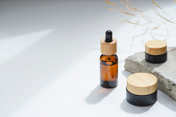 Amber glass dropper with bamboo lid and black jars. Bottle on grey concrete podium for product presentation. Skincare cosmetic with wildflowers. Beauty concept