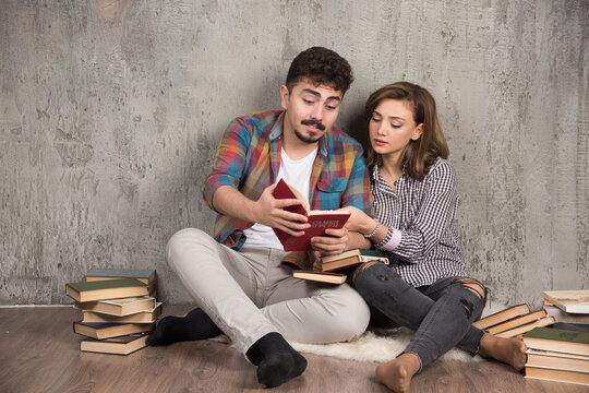 Lovely couple reading an interesting book while sitting on floor