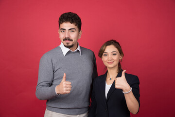 Two business partners giving thumbs up on red background