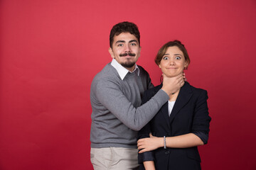 Young man playfully strangles woman on red background