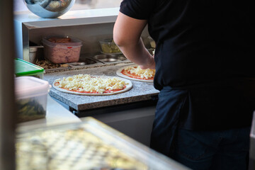 Unrecognizable male putting cheese on pizzas in a restaurant kitchen. Pizzeria.