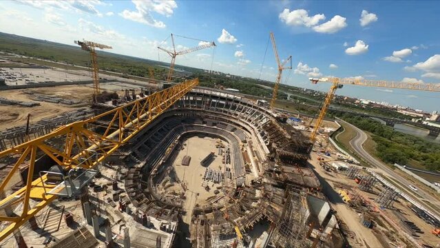 Assembling sports stadium with high cranes and professional workers at construction site in city on sunny day first point view