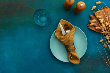 Table setting, empty plate with napkin and cutlery on turquoise background, top view of served table decorated with dry flowers