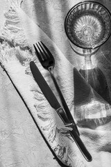 Table setting- cutlery, napkin and glass of drink  with strong shadows on the table. Minimal home decor. Black and white photography.