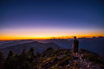 An athletic adventurous male hiker standing on top of a mountain looking out at a beautiful sunset.