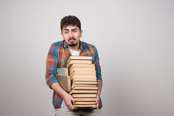 Exhausted male student trying to hold bunch of heavy books