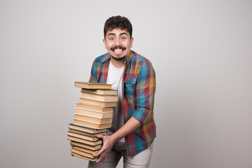 Young man holding bunch of books on gray background