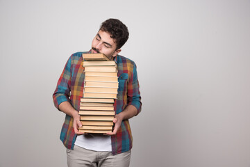 Young man holding a lot of books on a gray wall