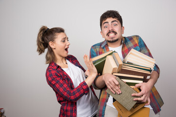 Young couple holding a lot of books on a gray wall