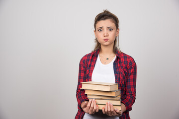 A young woman holding a stack of books on a gray wall