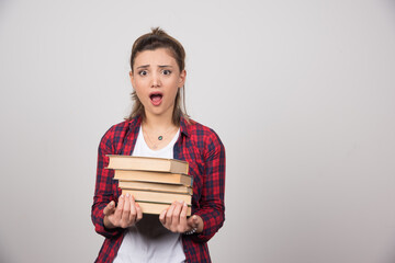 A shocked woman holding a stack of books on a gray wall